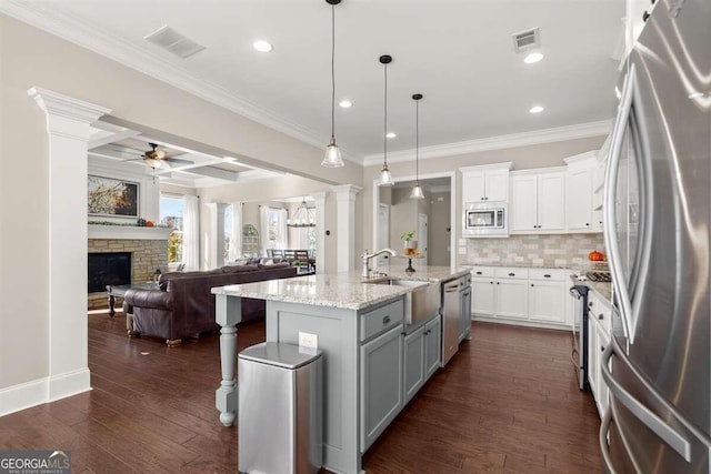 kitchen featuring appliances with stainless steel finishes, decorative columns, white cabinetry, and a center island with sink