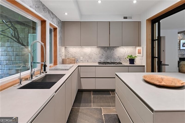 kitchen with gas cooktop, backsplash, gray cabinetry, and sink