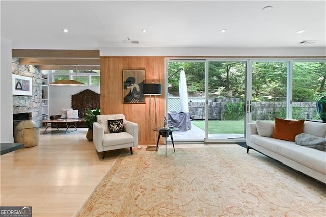 living room with light wood-type flooring, a stone fireplace, and a wealth of natural light