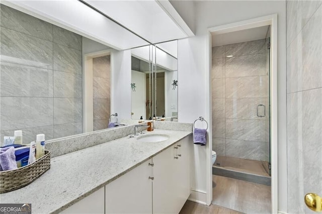 bathroom featuring a shower with door, vanity, wood-type flooring, and toilet