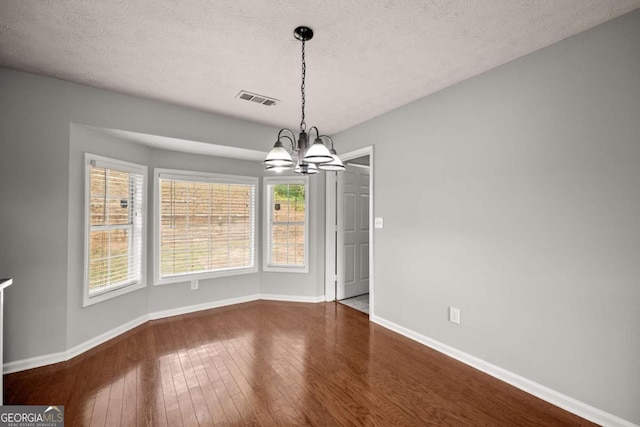 unfurnished dining area featuring hardwood / wood-style floors, a textured ceiling, and a notable chandelier