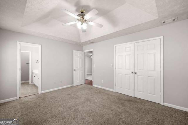 unfurnished bedroom with a textured ceiling, a tray ceiling, ceiling fan, and light colored carpet