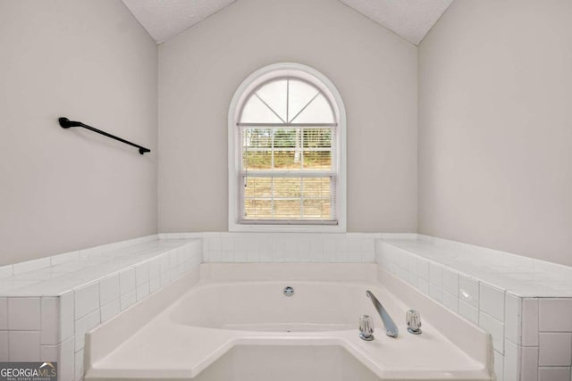 bathroom featuring vaulted ceiling, a bathtub, and a textured ceiling