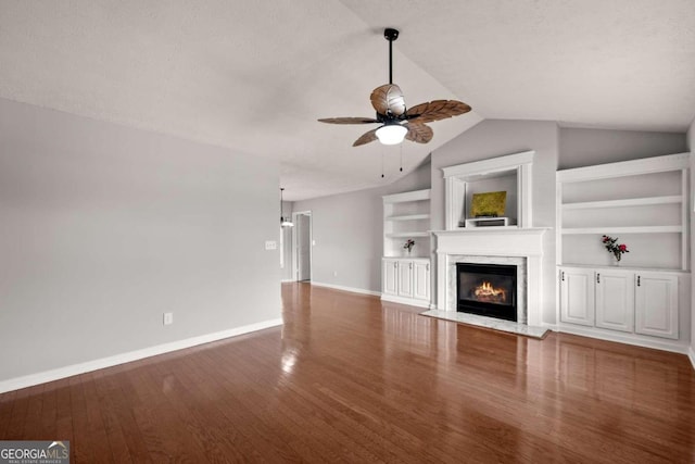 unfurnished living room featuring ceiling fan, built in features, a high end fireplace, wood-type flooring, and lofted ceiling