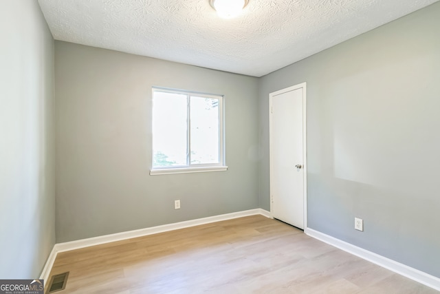 empty room with a textured ceiling and light hardwood / wood-style floors