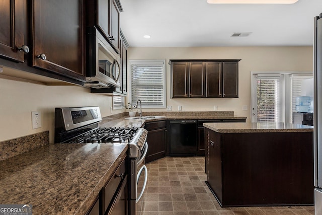 kitchen featuring appliances with stainless steel finishes, dark stone counters, dark brown cabinetry, sink, and a center island