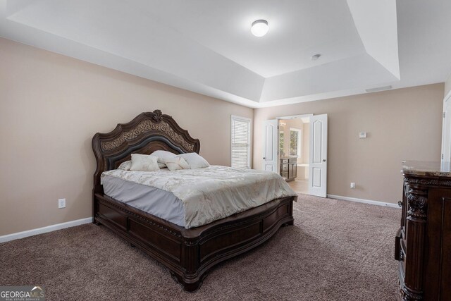 carpeted bedroom featuring a raised ceiling and connected bathroom