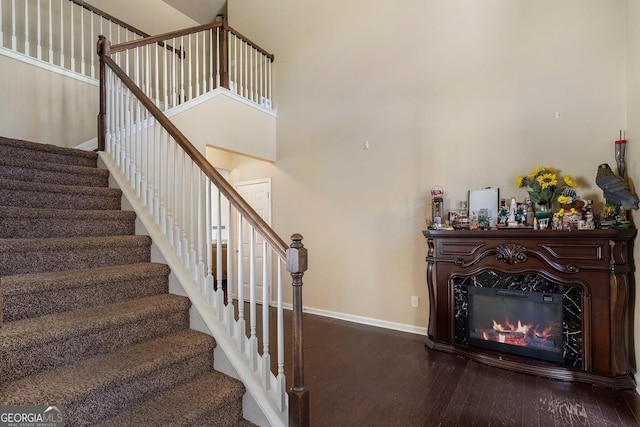 staircase featuring a premium fireplace, a towering ceiling, and hardwood / wood-style flooring