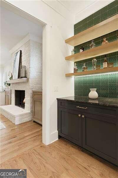 bar featuring light wood-type flooring, a fireplace, and tasteful backsplash