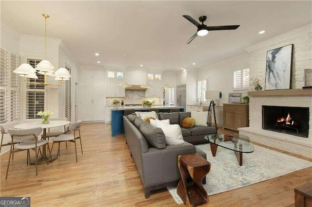 living room with a stone fireplace, ceiling fan, sink, and light hardwood / wood-style floors