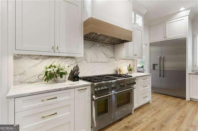 kitchen with white cabinets, light hardwood / wood-style floors, high quality appliances, and custom exhaust hood