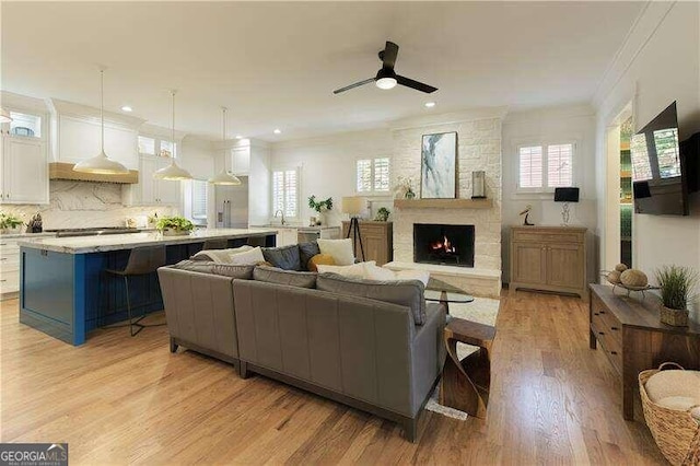 living room with ceiling fan, crown molding, sink, a fireplace, and light hardwood / wood-style floors