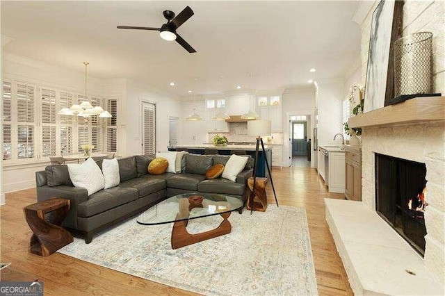 living room featuring ceiling fan with notable chandelier, light hardwood / wood-style floors, ornamental molding, and sink