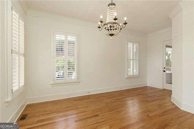 empty room with hardwood / wood-style floors, crown molding, and a chandelier