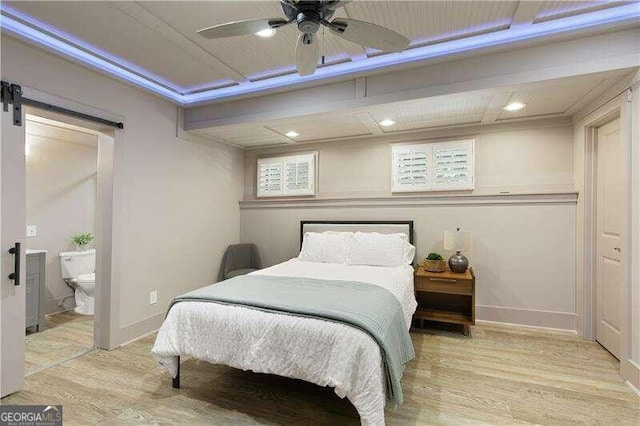 bedroom featuring ceiling fan, a barn door, light hardwood / wood-style floors, and connected bathroom