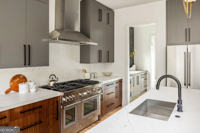 kitchen featuring sink, wall chimney exhaust hood, light wood-type flooring, premium appliances, and light stone counters