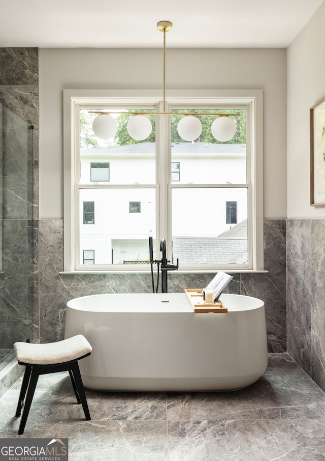 bathroom with a tub to relax in, a healthy amount of sunlight, and tile walls