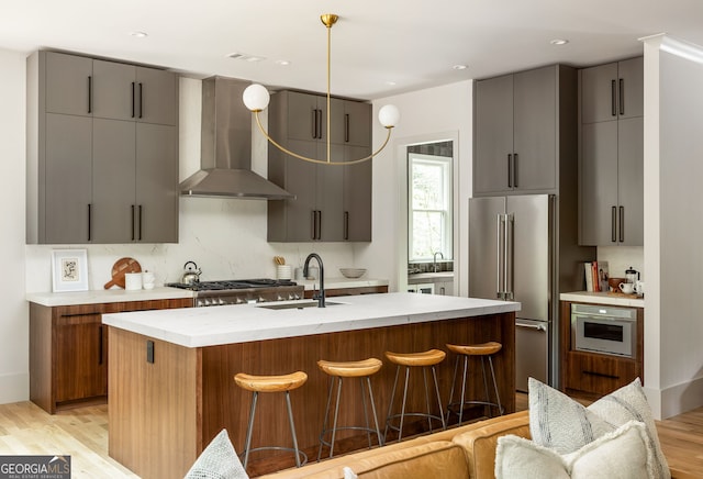 kitchen featuring a kitchen breakfast bar, stainless steel appliances, sink, wall chimney range hood, and light hardwood / wood-style flooring