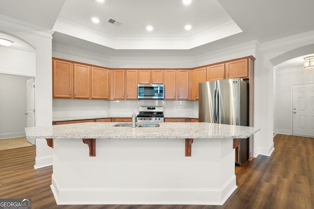 kitchen featuring dark hardwood / wood-style flooring, light stone countertops, a center island with sink, and stainless steel appliances