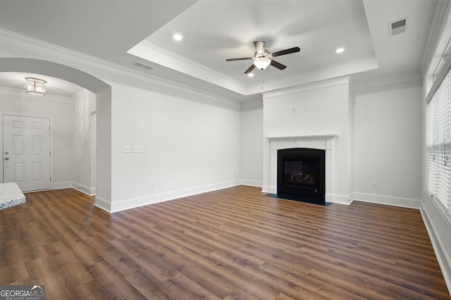 unfurnished living room featuring ceiling fan, crown molding, dark wood-type flooring, and a raised ceiling