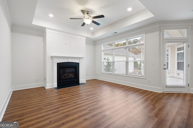 unfurnished living room featuring a raised ceiling, crown molding, ceiling fan, and dark hardwood / wood-style floors