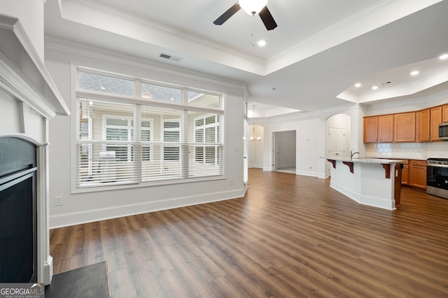 unfurnished living room featuring a tray ceiling, ceiling fan, crown molding, and dark hardwood / wood-style flooring