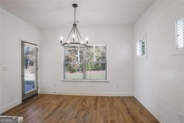 unfurnished dining area with an inviting chandelier and dark wood-type flooring