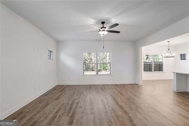 unfurnished living room with ceiling fan with notable chandelier and wood-type flooring