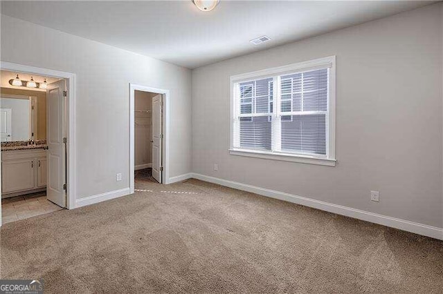 unfurnished bedroom featuring a closet, a spacious closet, light carpet, and ensuite bath