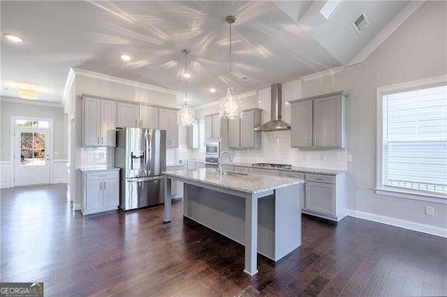 kitchen featuring wall chimney exhaust hood, stainless steel appliances, dark hardwood / wood-style floors, pendant lighting, and a center island with sink