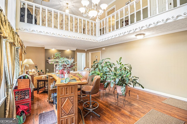 dining area with hardwood / wood-style flooring, a towering ceiling, ornamental molding, and an inviting chandelier