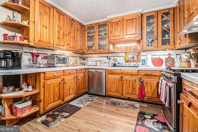 kitchen featuring appliances with stainless steel finishes, tile countertops, light wood-type flooring, ornamental molding, and a textured ceiling