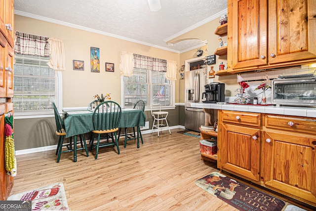 kitchen with crown molding, light hardwood / wood-style flooring, stainless steel refrigerator with ice dispenser, a textured ceiling, and tile countertops