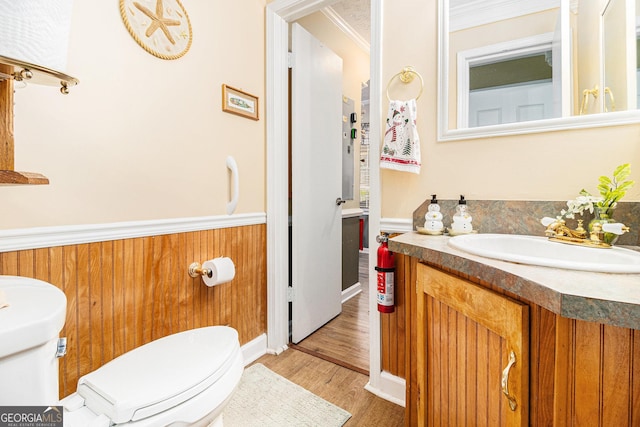 bathroom with wooden walls, hardwood / wood-style flooring, vanity, toilet, and crown molding