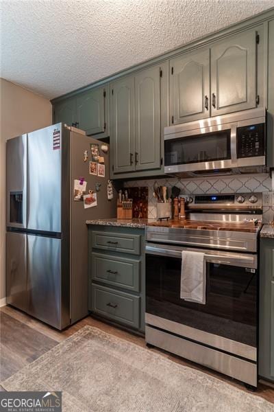 kitchen with appliances with stainless steel finishes, a textured ceiling, tasteful backsplash, and light hardwood / wood-style floors