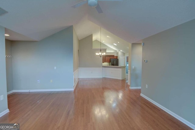 unfurnished living room with ceiling fan with notable chandelier, vaulted ceiling, and light hardwood / wood-style flooring