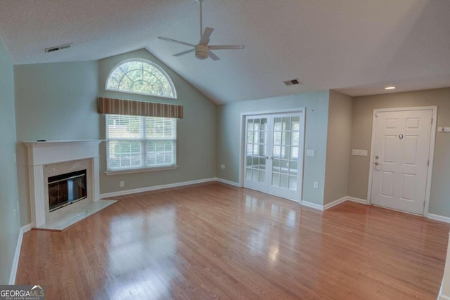 unfurnished living room with ceiling fan, a premium fireplace, a textured ceiling, vaulted ceiling, and light wood-type flooring