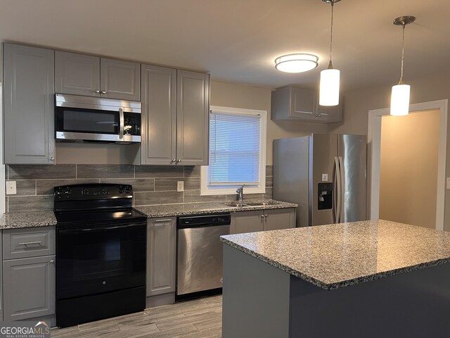 kitchen featuring backsplash, decorative light fixtures, gray cabinets, appliances with stainless steel finishes, and light wood-type flooring