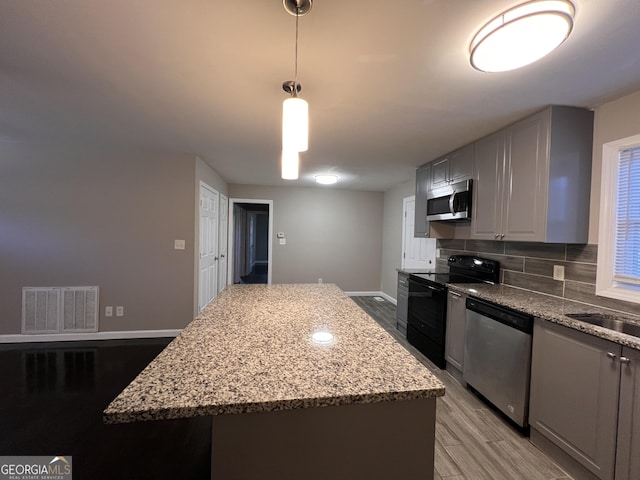 kitchen featuring appliances with stainless steel finishes, light wood-type flooring, a kitchen island, and pendant lighting