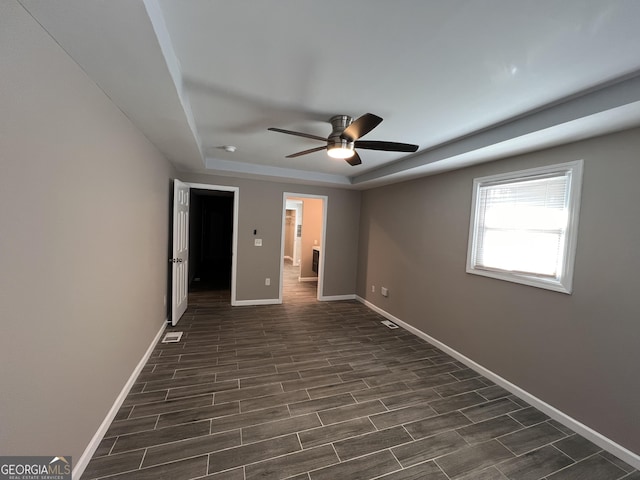 unfurnished room featuring dark hardwood / wood-style flooring, a tray ceiling, and ceiling fan