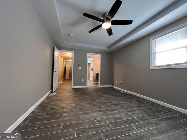 unfurnished bedroom with a raised ceiling, ceiling fan, and dark hardwood / wood-style flooring