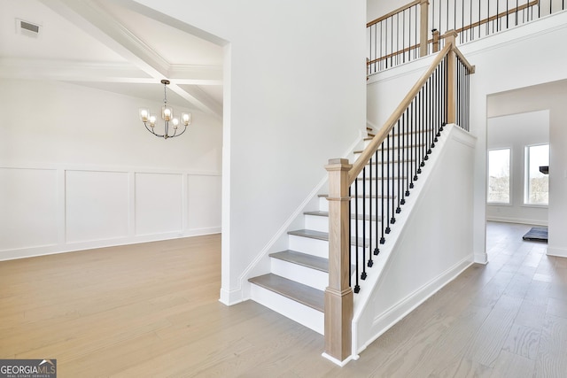 stairs featuring coffered ceiling, beam ceiling, hardwood / wood-style floors, and an inviting chandelier