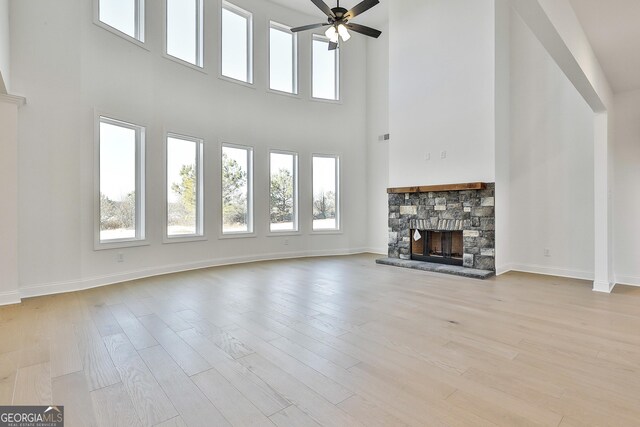 unfurnished living room featuring ceiling fan, a fireplace, a towering ceiling, and light wood-type flooring