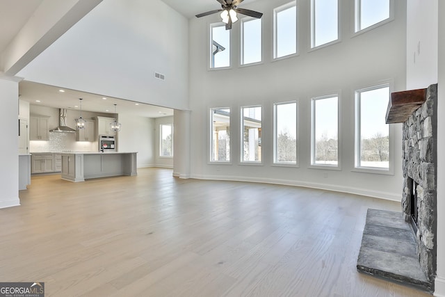 unfurnished living room featuring a high ceiling, light wood-type flooring, a stone fireplace, and plenty of natural light