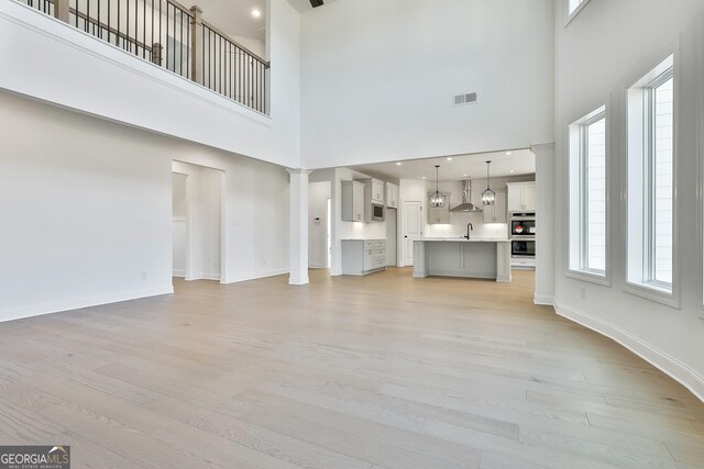 unfurnished living room featuring sink, a towering ceiling, and light hardwood / wood-style floors