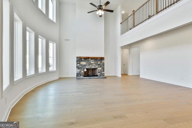 unfurnished living room featuring ceiling fan, a stone fireplace, a high ceiling, and light hardwood / wood-style flooring