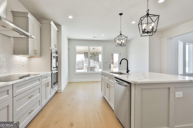 kitchen with a center island with sink, sink, wall chimney exhaust hood, appliances with stainless steel finishes, and decorative light fixtures