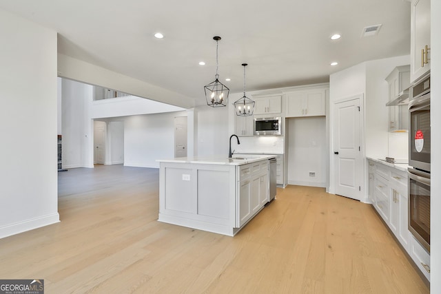 kitchen with pendant lighting, white cabinets, light wood-type flooring, an island with sink, and appliances with stainless steel finishes