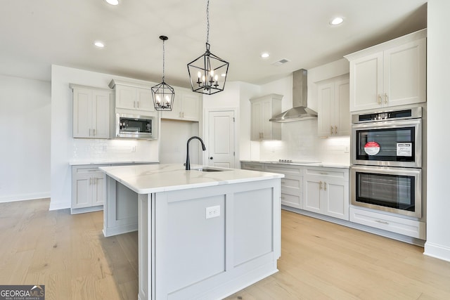 kitchen featuring built in microwave, sink, wall chimney exhaust hood, double oven, and a kitchen island with sink