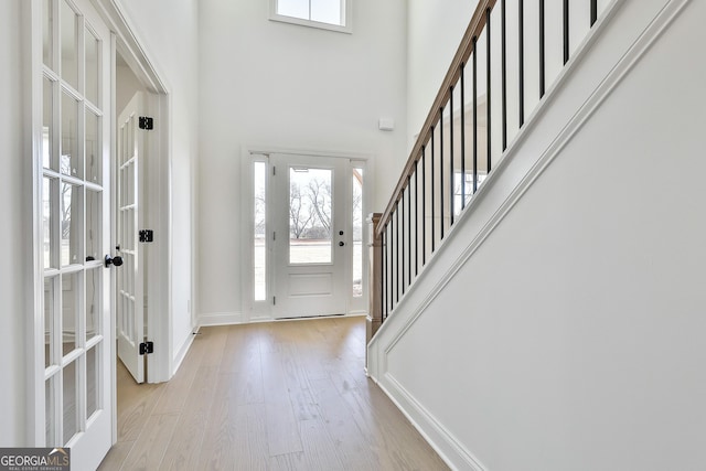 foyer with light hardwood / wood-style flooring, a towering ceiling, and french doors